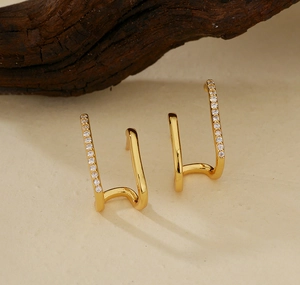 Makro-Detail von asymmetrischen Doppelschicht-Goldohrringen mit glitzernden Zirkonsteinen