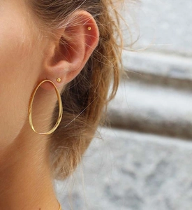 Gros plan sur les boucles d'oreilles ovales torsadées dorées et clous sphériques