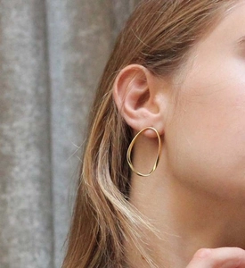 Gros plan de boucles d'oreilles ovales dorées torsadées portées par un mannequin