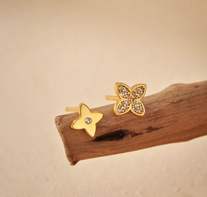 Detail of asymmetric flower stud earrings with gold plating and cubic zirconia on wood