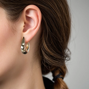 Polished golden S925 silver thick teardrop hoop earrings on female model's ear