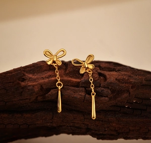 Macro shot of 18K gold butterfly earrings with long tassel teardrop pendants on wood