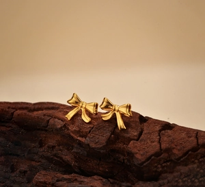 Gros plan de boucles d'oreilles nœuds dorées sur texture boisée et lumière douce