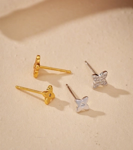 Macro shot of gold and silver four-leaf clover earrings with zircon inlay on stone surface