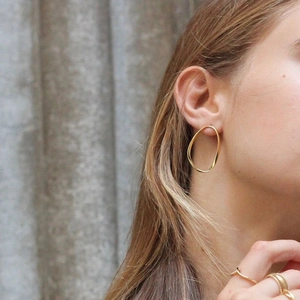 Boucles d'oreilles ovales torsadées en argent S925 et bagues dorées sur un mannequin