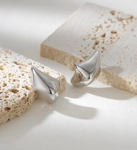 Detailed macro view of glossy silver teardrop earrings on minimalist travertine stone