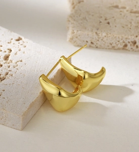 Close-up of elegant gold plated U-shaped earrings on textured travertine stone