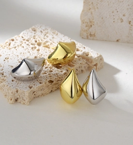Macro view of gold and silver irregular teardrop earrings on natural beige stone