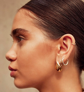 Close-up of a model wearing stacked irregular liquid metal gold earrings and hoops
