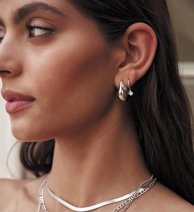 Close-up of layered silver necklaces and teardrop earrings on a model showing rich texture