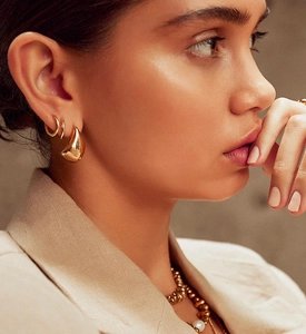 Detailed view of polished gold teardrop stud earring and hoop on a female model