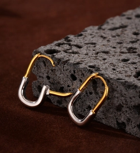 Macro detail of geometric U-shaped earrings in polished gold and silver contrast finish
