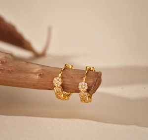 Dettaglio di orecchini a cerchio a fiore dorati con micro-pave di cristalli su legno