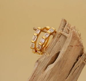 Détail de boucles d'oreilles huggie dorées avec zircons baguette sur une branche