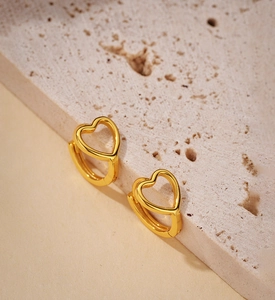 Primo piano di orecchini a cerchio dorati a forma di cuore su una superficie di pietra