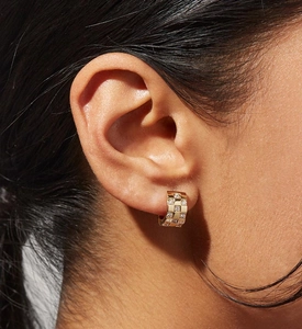 Close-up of a model wearing a gold huggie hoop earring with checkered micro-pave crystals