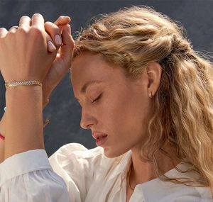 Gros plan d'un collier doré à damier et de créoles assorties portés par un mannequin