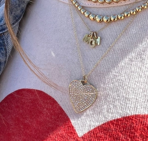 Detail von geschichteten Goldketten mit MOM-Anhänger und kristallbesetztem Herz