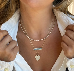 Nahaufnahme der dreilagigen Goldkette mit Herzanhänger und blauem Opal-Detail