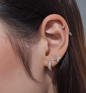 Macro shot of gold-plated butterfly stud and pavé crystal hoop earrings on model