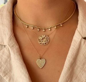 Detailaufnahme dreischichtiger Goldhalsketten mit Glücksbringern und Herzanhängern
