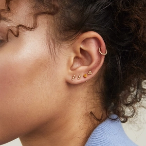 Detailopname van een model met een set gouden kralenoorbellen en een bijpassende ear cuff