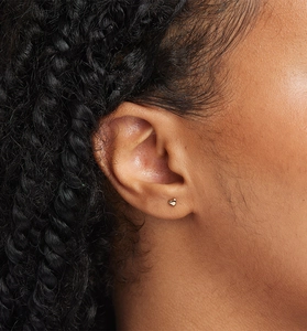 Close-up of a minimalist heart-shaped gold stud earring worn on a model's ear