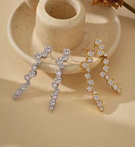 Detail of silver and gold curved drop earrings with round zircons on ceramic holder