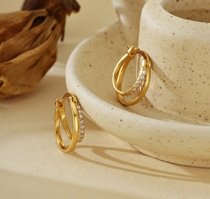 Close-up of gold double-layer hoop earrings with inlaid zircons on a ceramic cup
