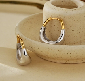 Vue détaillée de boucles d'oreilles bicolores or et argent sur plateau céramique