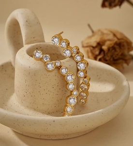 Detailed view of gold irregular earrings with pavé set white zircon stones on ceramic tray