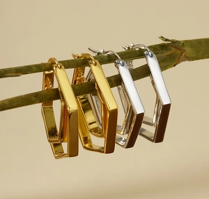 Detail of geometric double hoop earrings in gold and silver finish hanging on a green branch