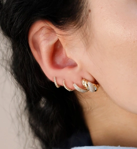 Close-up of stacked 18K gold-plated twisted hoops and zircon stud earrings on model ear