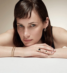 Close-up of model wearing hexagonal 18K gold earrings and black agate rings