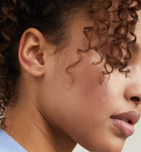 Close-up of elegant gold triple-bead stud earrings worn on ear for a minimalist look