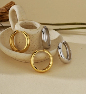 Minimalist high-polished silver and gold hoop earrings on a neutral textured background