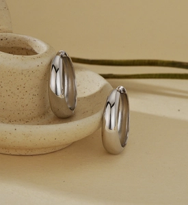 Close-up of chunky silver hoop earrings leaning on ceramic dish with dried flowers