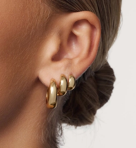 Close-up of three graduated polished gold hoop earrings worn on model's ear
