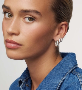 Three sizes of polished silver hoop earrings stacked on model for a trendy look