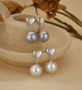 Detail of silver heart stud earrings with grey and white pearl pendants in a cozy setting