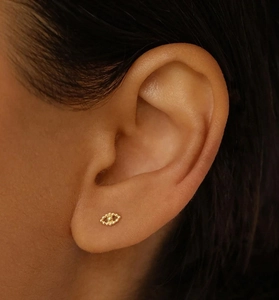 Close-up of golden eye-shaped stud earring with granular texture on earlobe