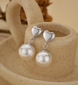 Close-up of S925 silver heart stud earrings with round white pearl drops on a ceramic cup