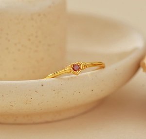 Detail of minimalist gold heart ring with red gemstone on ceramic tray background