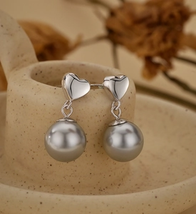 Detailed view of silver heart earrings with grey shell pearls on a ceramic cup rim