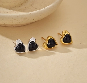 Macro view of silver and gold heart stud earrings featuring elegant black onyx inlay