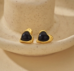 Detailed view of heart-shaped black agate stud earrings on a beige ceramic display stand
