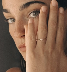 Detail shot of a minimalist gold heart ring with micro diamond on woman finger