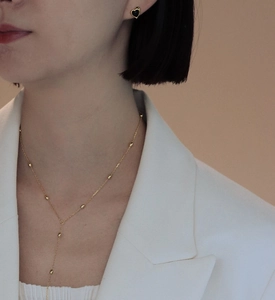 Detail of elegant gold Y-necklace and black heart studs on a woman in a white suit