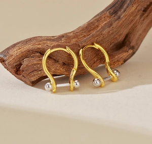 Detailweergave van tweekleurige U-vormige metalen oorringen op een houten decor