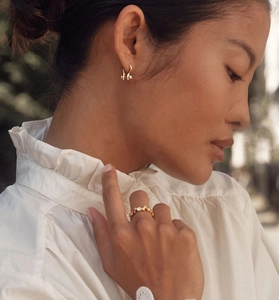 Detailopname van een vrouw met goudkleurige oorringen en een dunne fonkelende diamanten ring